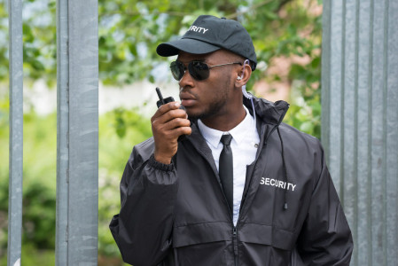 Security Guard Using Walkie-Talkie. Young Male Security Guard In Black Uniform Using Walkie-Talkie